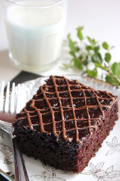 a piece of chocolate cake on a plate next to a fork and glass of milk