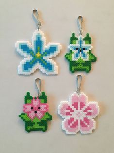 four cross stitch flower ornament hangings on a white table with one pink, one blue and one green