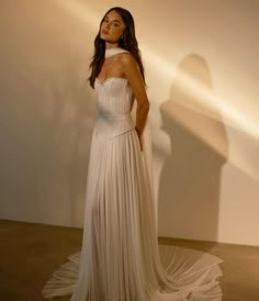 a woman standing in front of a white wall wearing a dress with pleated skirt