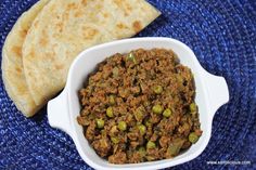 a white bowl filled with meat and peas next to a flatbread on a blue mat