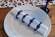 a white plate topped with blue beads next to a wine glass and napkin on top of a wooden table