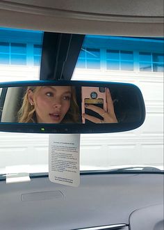 a woman taking a selfie in the rear view mirror of a car while holding a camera