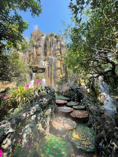 a waterfall surrounded by lush green trees and flowers