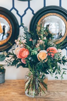 a vase filled with flowers sitting on top of a wooden table next to two mirrors