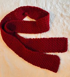 a red knitted scarf laying on top of a white bed sheet with a knot at the end