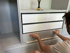 a man sitting on the floor next to a white dresser with drawers and shelves in front of him