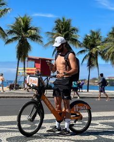 a shirtless man standing next to a bike on the street with palm trees in the background