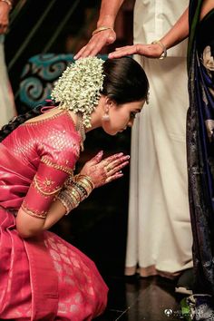 a woman in a pink sari kneeling down with her hands on her face and other people around her