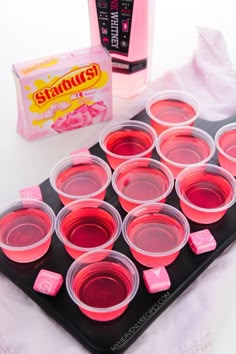 pink jello cups are lined up on a tray next to a bag of candy