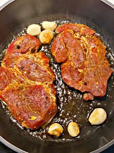 two pieces of meat cooking in a frying pan with garlic and pepper on the side