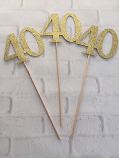 gold glitter number 40 cake toppers on a white brick wall with the number forty