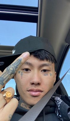 a man with tattoos on his face sitting in the back seat of a car holding up a pen to his forehead