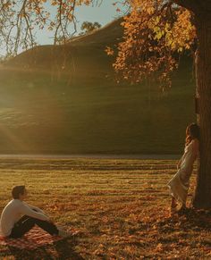 a man and woman sitting on a blanket under a tree with the sun behind them