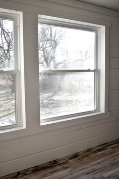 two windows in the corner of a room with wood flooring and white painted walls