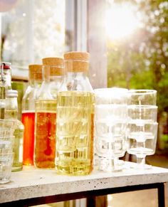 several bottles and glasses are lined up on a table in front of an open window