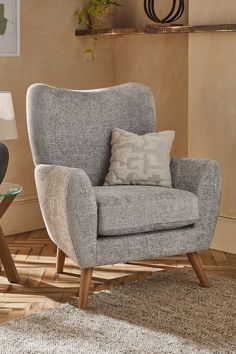 a gray chair sitting on top of a wooden floor next to a table with a lamp