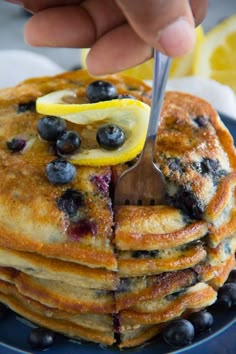 a person cutting into a stack of pancakes with blueberries and lemons on top