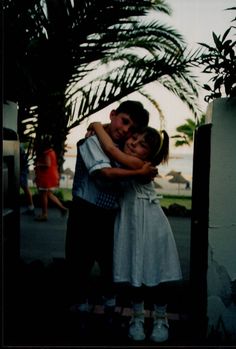 two people hugging each other in front of palm trees