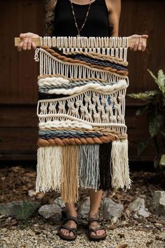 a woman standing in front of a wall hanging with different types of yarn on it