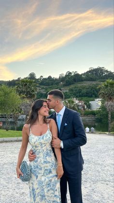 a man and woman standing next to each other in front of a body of water