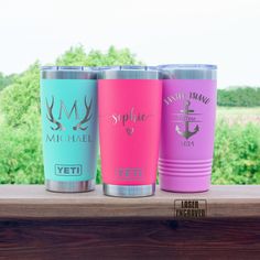 three different colored yeti cups sitting on a window sill with trees in the background