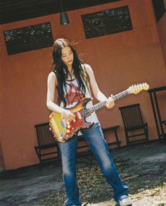 a girl with long hair is playing an electric guitar in front of a red building