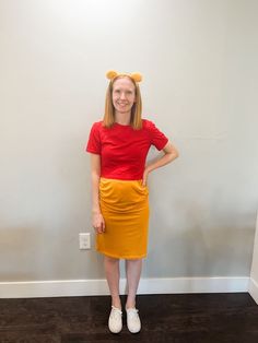 a woman standing in front of a white wall wearing a red shirt and yellow skirt