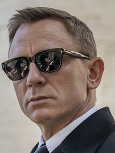 a man in a suit and sunglasses looks off into the distance with his head tilted to the side