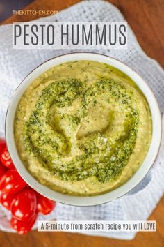 pesto hummus in a white bowl with tomatoes on the side and text overlay