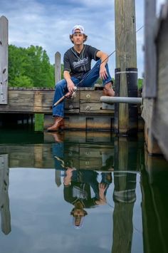 a man sitting on top of a wooden dock next to water with a fishing pole