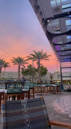 an outdoor seating area with palm trees and colorful sky in the background at sunset or dawn