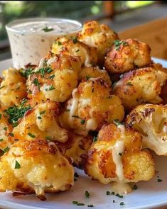 a white plate topped with cooked cauliflower next to a bowl of ranch dressing