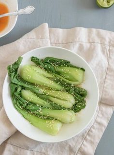 a white bowl filled with green vegetables on top of a table next to a cup