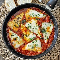 an iron skillet filled with cheese and sauce on top of a woven place mat