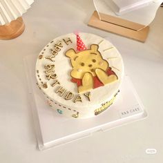 a winnie the pooh birthday cake is sitting on a white table with a wooden stand