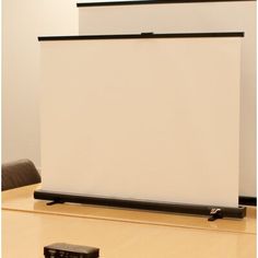 an empty conference room with a projector screen and remotes on the table in front of it