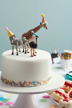 two giraffes and a zebra on top of a white cake with sprinkles