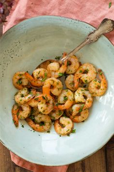 a white bowl filled with cooked shrimp and garnished with parsley