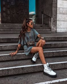 a woman sitting on some steps with her legs crossed and wearing white converses, looking off to the side