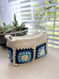 a crocheted purse sitting on top of a table next to a potted plant