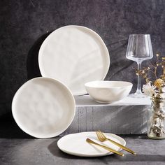 white plates and silverware are sitting on a table next to a vase with flowers