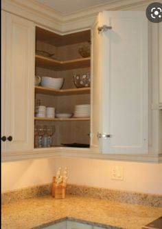 an open cabinet in the corner of a kitchen with granite counter tops and white cabinets