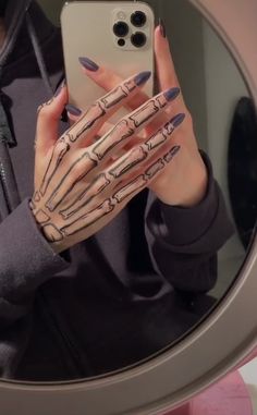 a woman holding up her cell phone in front of a mirror with skeleton hands on it