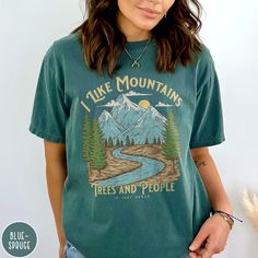 a woman wearing a t - shirt that says i like mountains trees and people