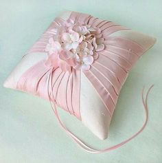 a pink and white pillow with flowers on the front is sitting on a light blue surface