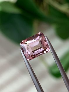 a pink diamond sitting on top of a piece of metal with a green plant in the background