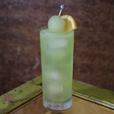 a green drink with an orange slice on the rim and a straw sticking out of it