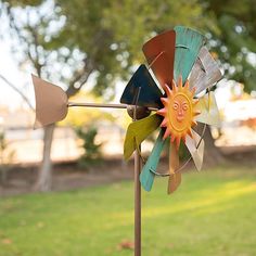 a colorful wind spin sitting on top of a green grass covered park bench next to a tree