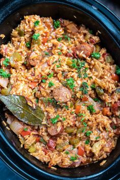 a black bowl filled with rice and sausage on top of a blue cloth next to a wooden spoon