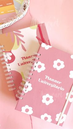 a pink planner with white flowers on it next to a basket full of notes and pens